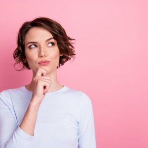 Thoughtful woman against pink background considering DiamondGlow® vs. Hydrafacial™ treatments for radiant, rejuvenated skin