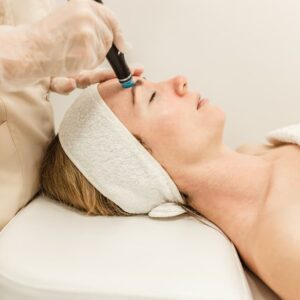 A woman receiving a HydraFacial treatment as a provider uses the device on her forehead during a professional skincare session.