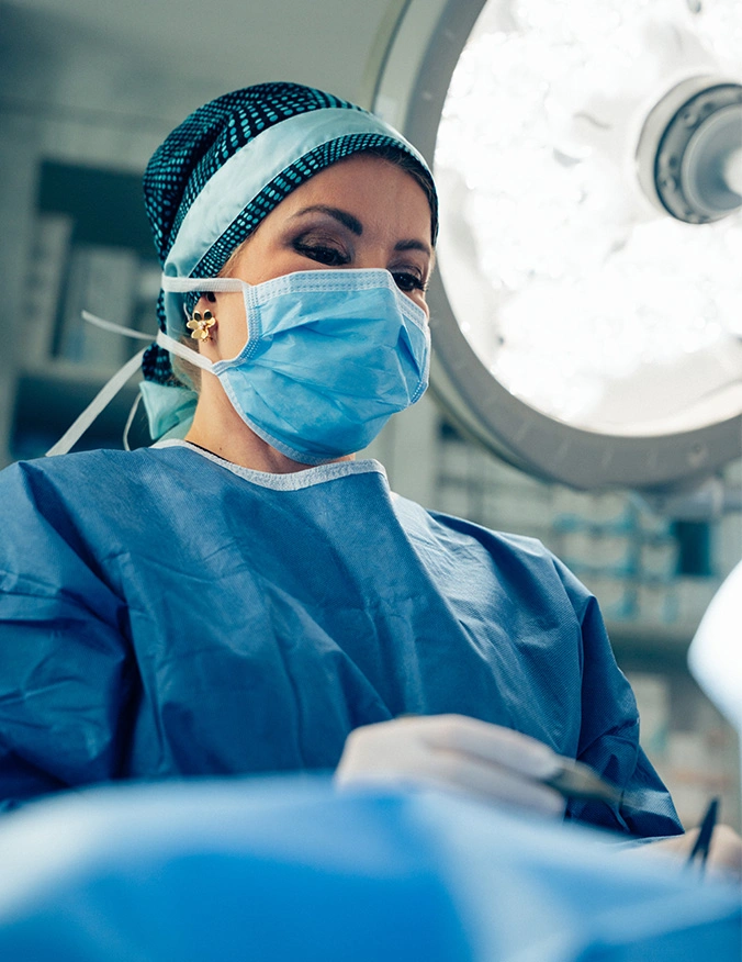 Female surgeon in blue scrubs and mask performing operation under surgical lights in operating room - Brow lift in Newport Beach, CA