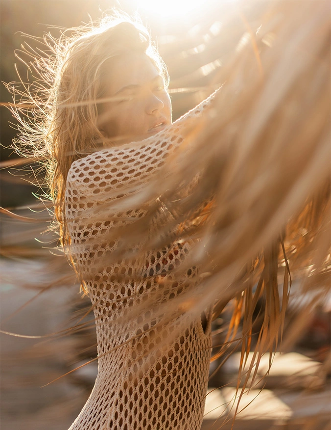 Woman in white mesh top sitting on beach at sunset with golden light and flowing hair - CoolSculpting in Newport Beach, CA