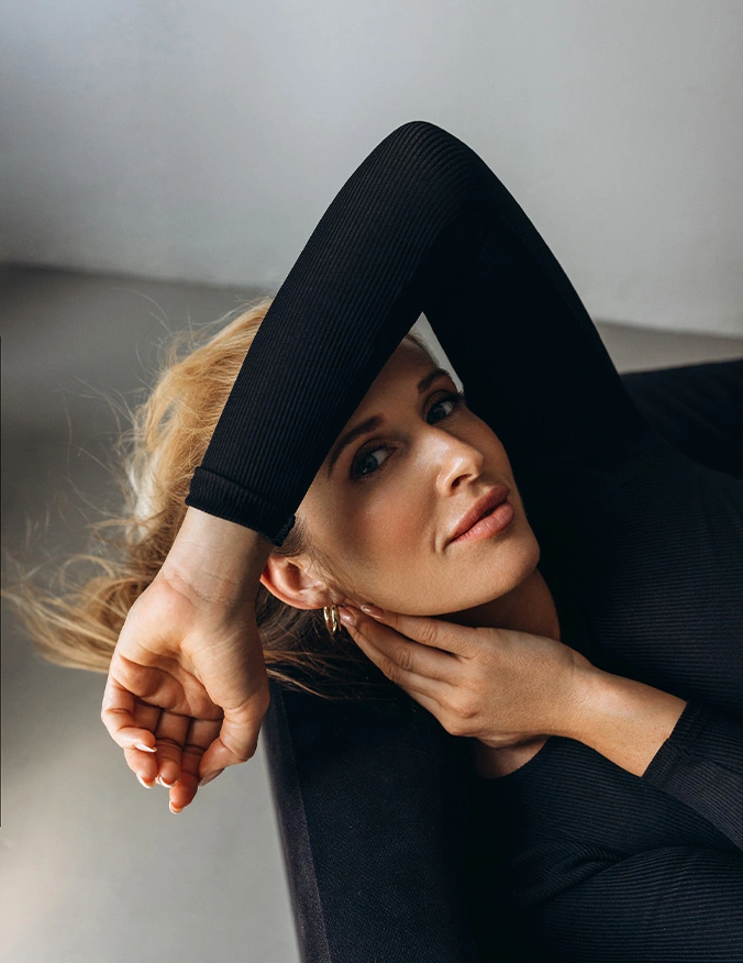 Woman in black turtleneck with blonde hair posing with arms above head in artistic portrait - Lip lift in Newport Beach, CA
