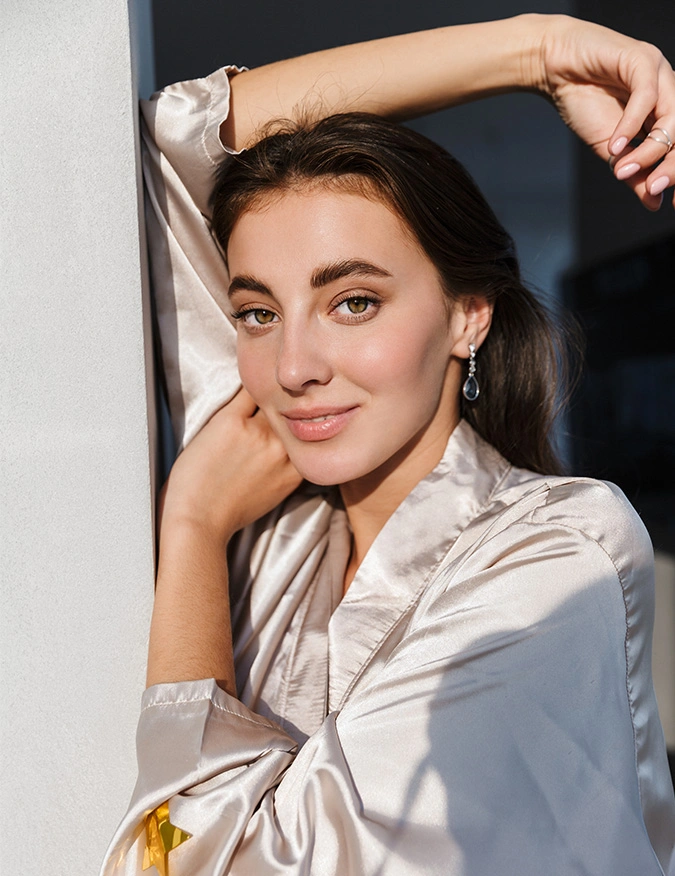 Professional woman in white blazer posing confidently with hand near face in modern studio portrait - microneedling in Newport Beach, CA