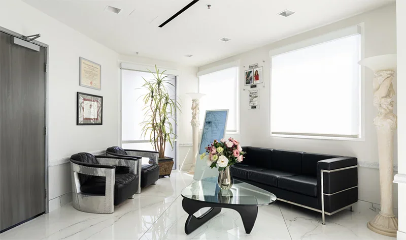 Modern minimalist office waiting area with black leather furniture, glass coffee table, and white tile flooring