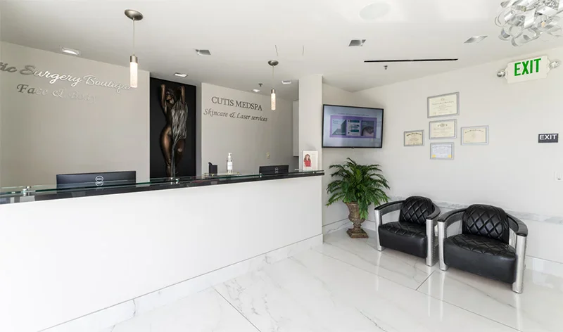 Modern white reception area with desk, black leather seating, plants, and exit sign for professional office contact