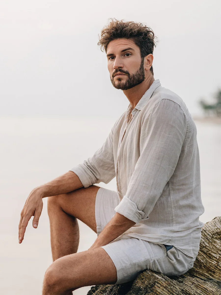 Man in white linen shirt sitting outdoors on beach at sunset in relaxed casual style - male in Newport Beach, CA