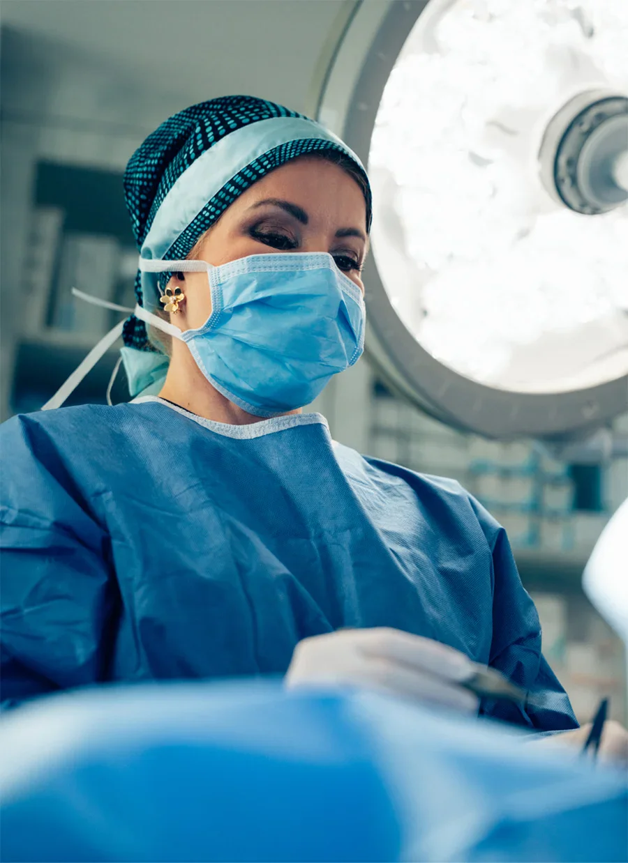 Doctor Bayati in blue scrubs and mask performing procedure in operating room with surgical lights