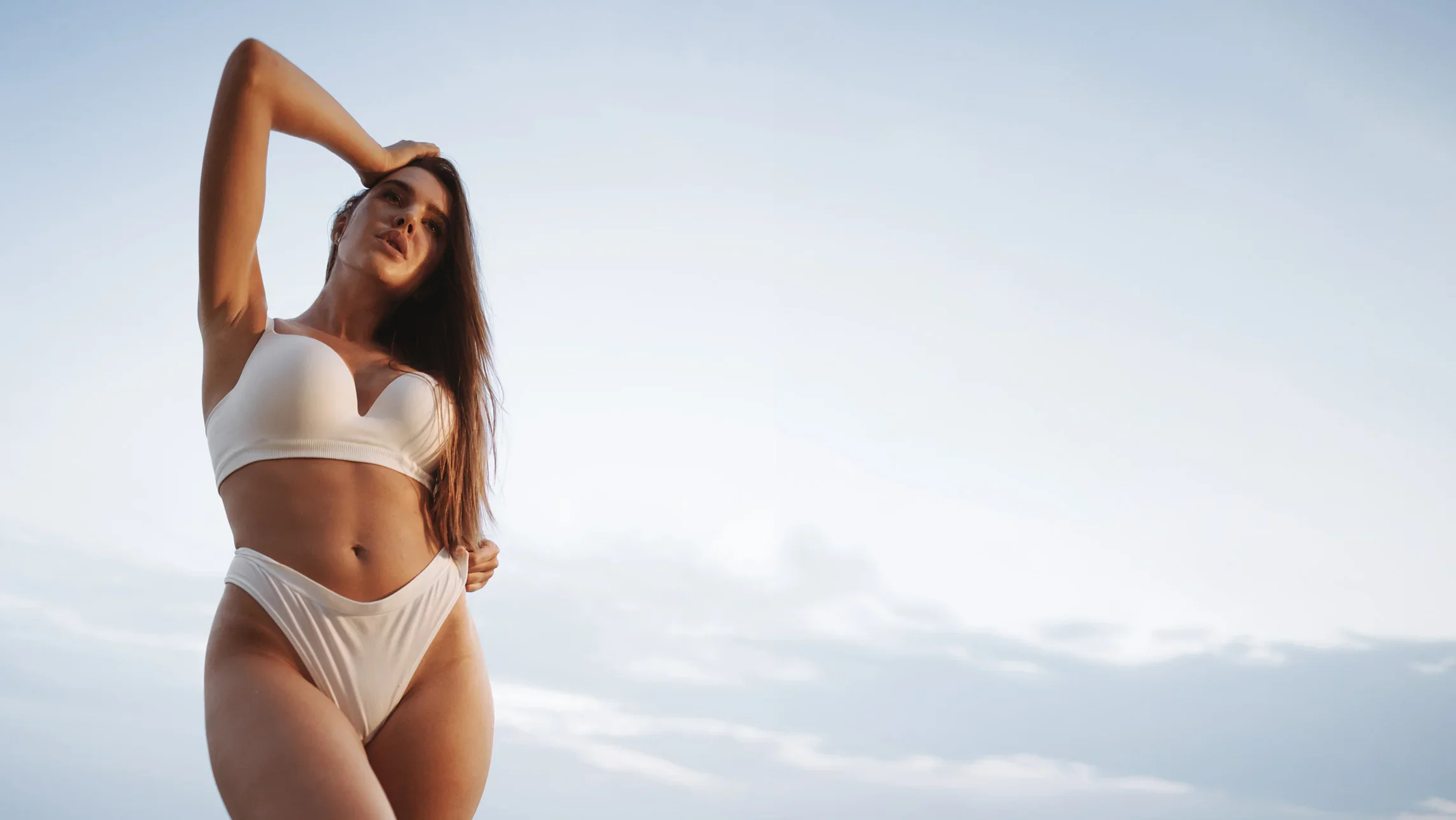 Woman in white swimwear posing by ocean on sunny day with clear blue sky - Vaginal rejuvenation in Newport Beach, CA