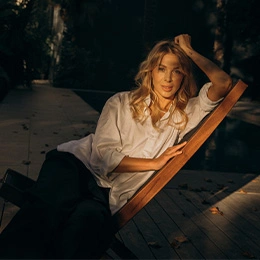 Woman in white shirt relaxing on wooden deck chair outdoors at golden hour - Chemical peels in Newport Beach, CA