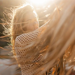 Woman in knit shawl enjoying golden hour sunset with windswept hair in wheat field - Coolsculpting in Newport Beach, CA