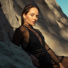 Woman in elegant black sheer dress posing against rocky coastal landscape at golden hour - Dermaplaning in Newport Beach, CA