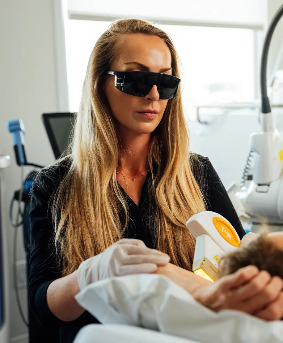 Lindsay short wearing sunglasses looking at a patients face as they lay down on a operating chair.