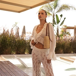 Woman in beige knit crop top and sheer pants carrying woven bag at tropical resort poolside - Liposuction in Newport Beach, CA