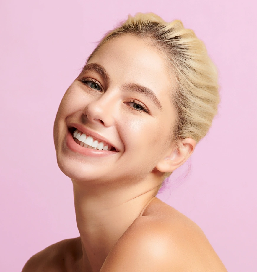 Smiling woman with glowing skin and white teeth on pink background showcasing beauty and dental care results - microneedling in Newport Beach, CA