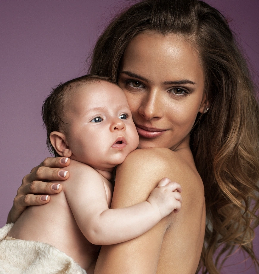 Mother lovingly holding baby against purple background in professional portrait photo - mommy makeover in Newport Beach, CA