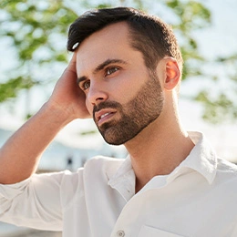 Thoughtful man with beard in white shirt looking away outdoors in natural lighting - otoplasty in Newport Beach, CA