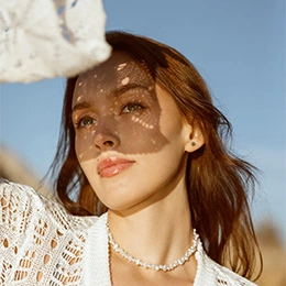 Woman wearing white lace top and pearl necklace in bright sunlight with dappled shadow patterns on face - Rhinoplasty in Newport Beach, CA
